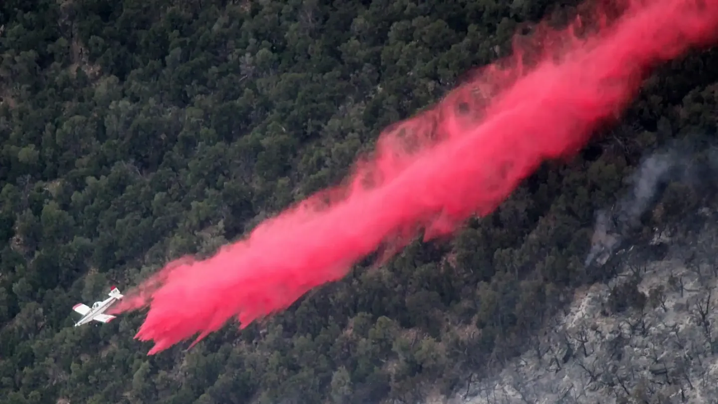 Air tanker dropping red retardant along a forested slope