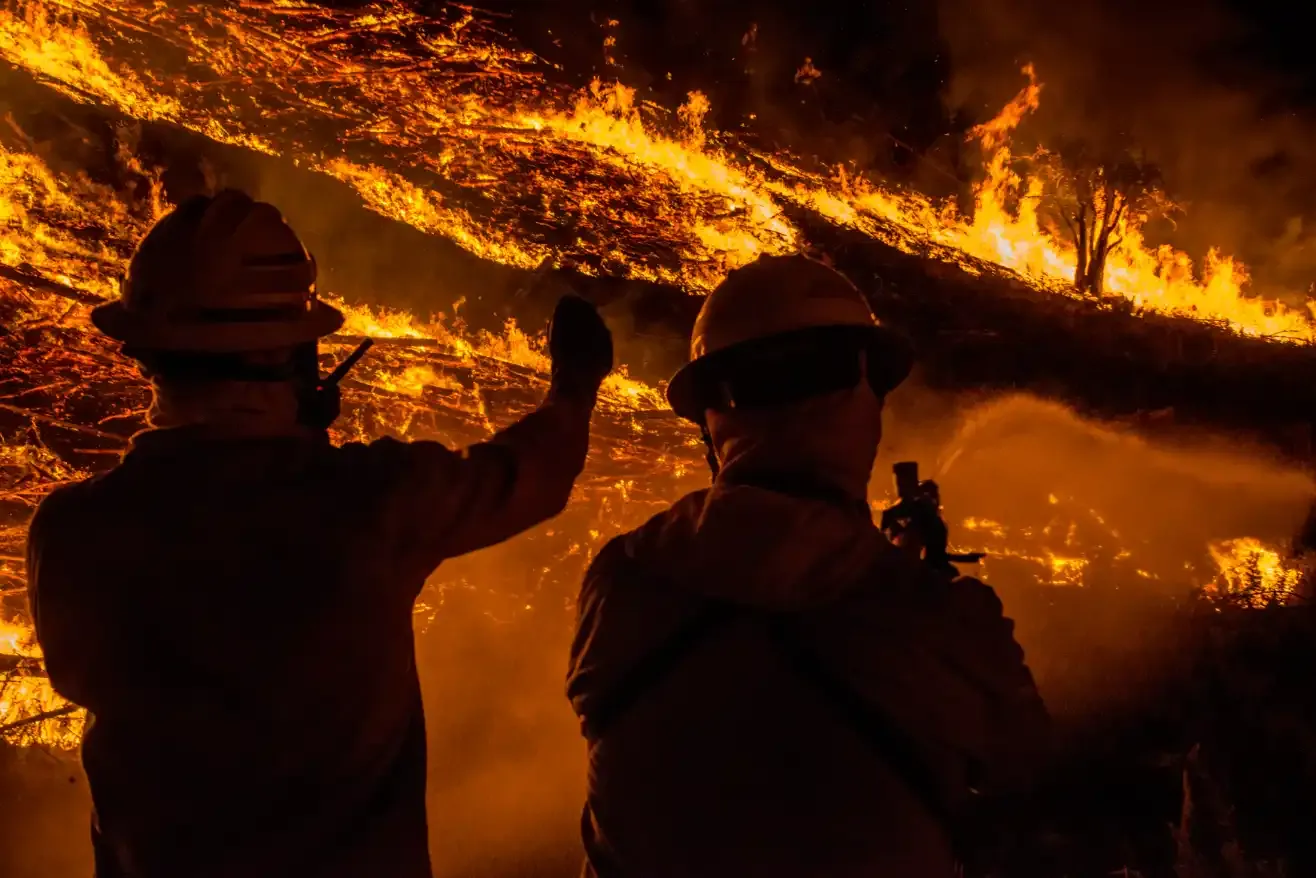 Two firefighters watching a fire burn across a hillside
