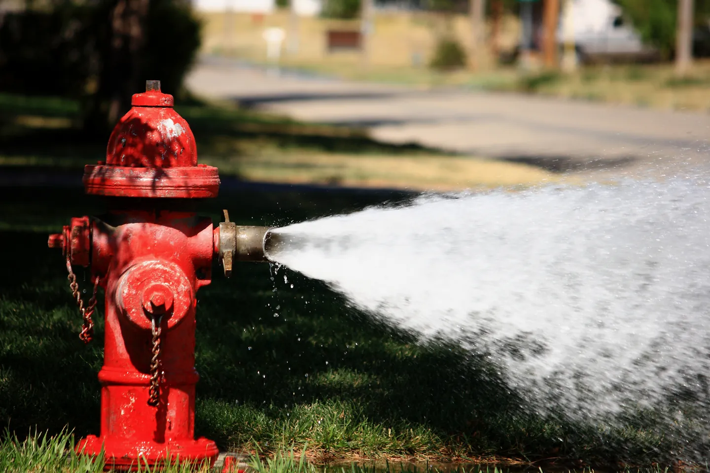 Red hydrant discharging water across the edge of a lawn
