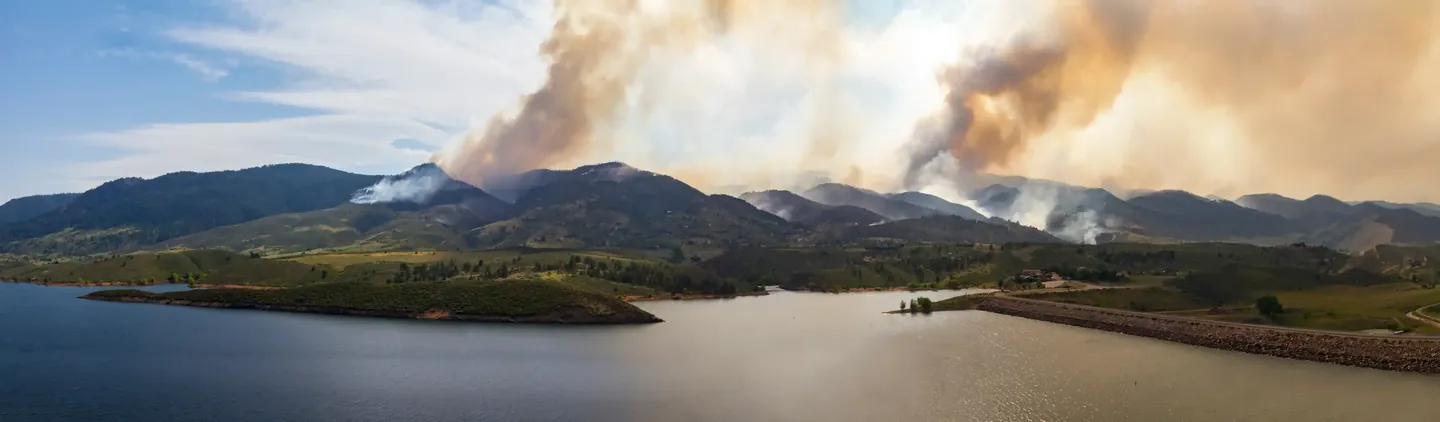 Wide view of smoke rising from mountains beyond a lake